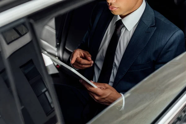 Visão cortada do empresário afro-americano usando tablet digital no carro — Fotografia de Stock