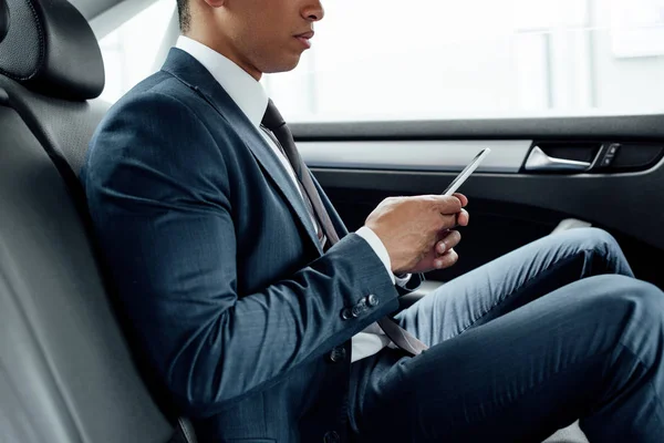 Vue partielle d'un homme d'affaires afro-américain utilisant un smartphone en voiture — Photo de stock