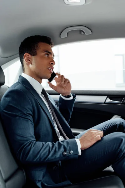 African american businessman in suit talking on smartphone in car — Stock Photo