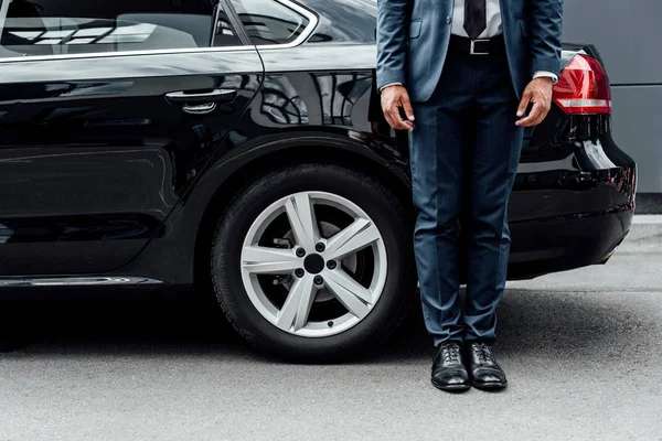 Vista recortada de hombre afroamericano en traje de pie cerca de coche negro - foto de stock