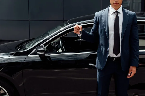 Vista recortada del hombre afroamericano en traje sosteniendo la llave del coche - foto de stock