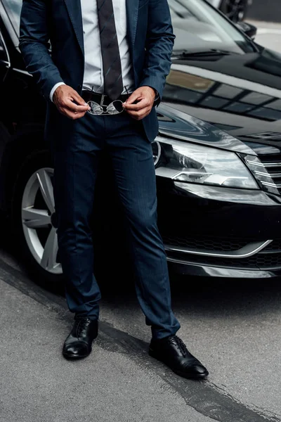 Cropped view of african american man in suit holding sunglasses near car — Stock Photo