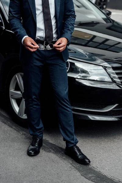 Vue recadrée de l'homme afro-américain en costume tenant des lunettes de soleil près de la voiture — Photo de stock