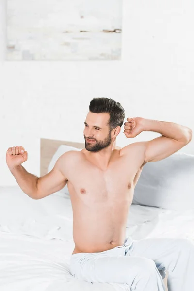 Schöner Mann dehnt sich auf Bett während des Morgens im Schlafzimmer — Stockfoto