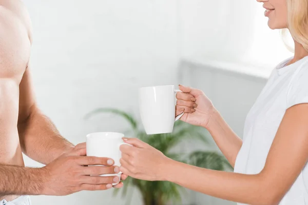 Vista recortada de pareja con tazas de café en casa por la mañana - foto de stock