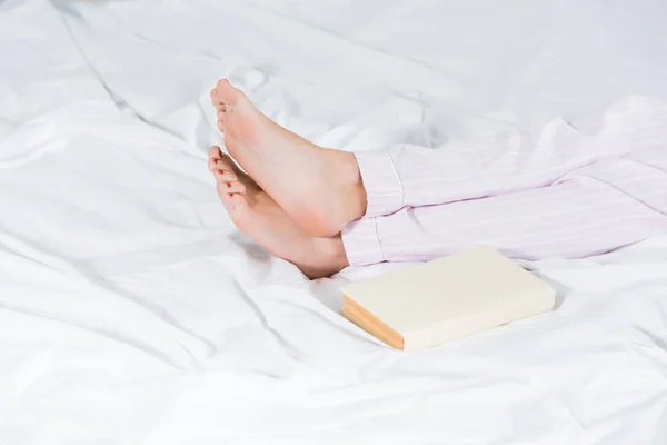 Vista recortada del hombre en pijama acostado en la cama cerca del libro - foto de stock