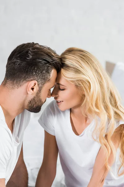 Hermosa pareja en camisetas blancas tocando con la frente en casa - foto de stock