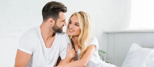 Panoramic shot of beautiful couple in pajamas hugging on bed at home — Stock Photo