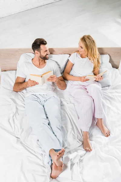 Belo casal sorridente deitado na cama com livros em casa — Fotografia de Stock