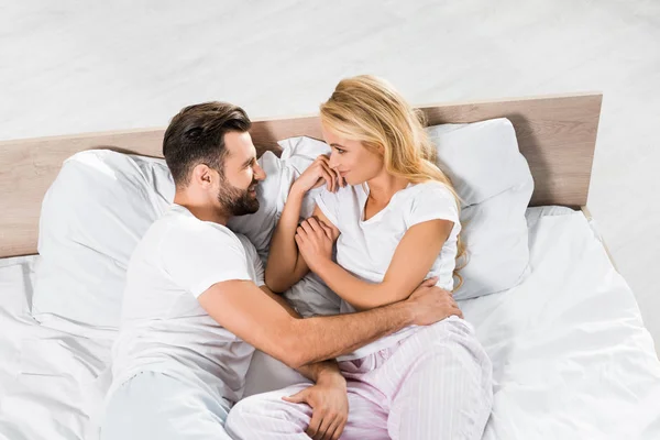 Высокий угол зрения на красивую пару, лежащую в постели и обнимающую дома — стоковое фото