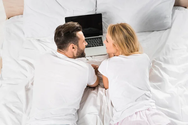 Vue arrière du couple couché au lit et utilisant un ordinateur portable à la maison — Photo de stock