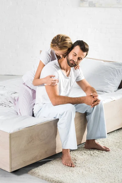 Beautiful couple in pajamas hugging on bed at home — Stock Photo