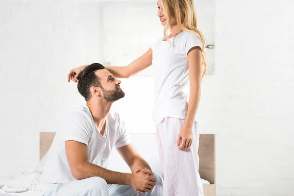 Beautiful woman in pajamas stroking man in bedroom with sunlight — Stock Photo
