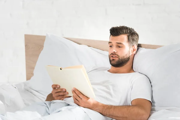 Schöner Mann, der morgens im Bett liegt und Buch liest — Stockfoto