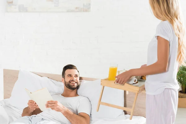 Mujer trayendo desayuno a hombre feliz en la cama por la mañana - foto de stock
