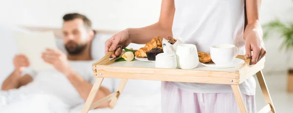 Tiro panorâmico de mulher segurando bandeja de comida com café da manhã no quarto — Fotografia de Stock