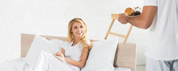 Plano panorámico del hombre llevando el desayuno a la mujer en la cama por la mañana - foto de stock