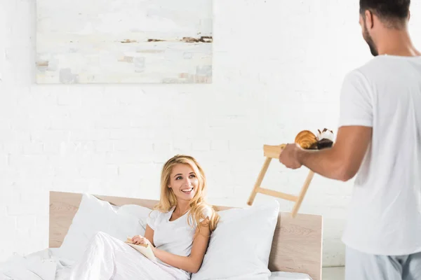 Hombre trayendo el desayuno a la mujer feliz en la cama por la mañana - foto de stock