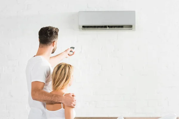 Vue arrière du couple avec télécommande souffrant de chaleur sous climatiseur à la maison — Photo de stock