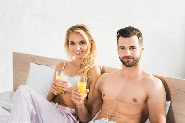 Пара в піжамі з апельсиновим соком в ліжку вранці — стокове фото