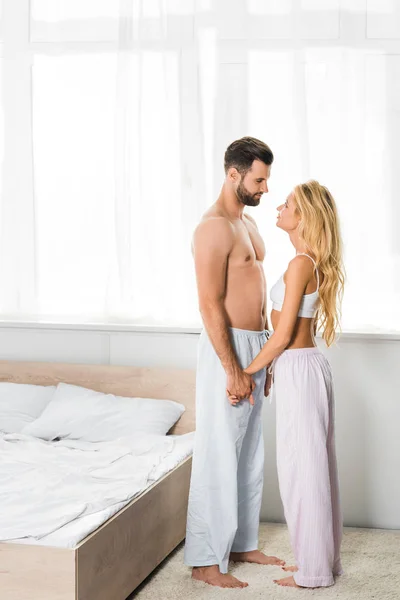 Красива пара в піжамі тримає руки вдома в спальні — стокове фото
