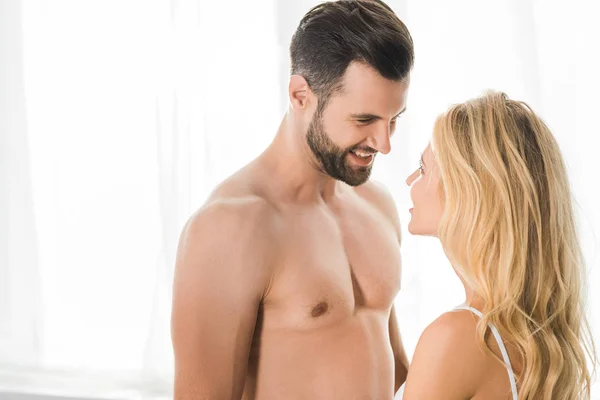 Guapo sonriente hombre sin camisa mirando a la mujer en casa - foto de stock