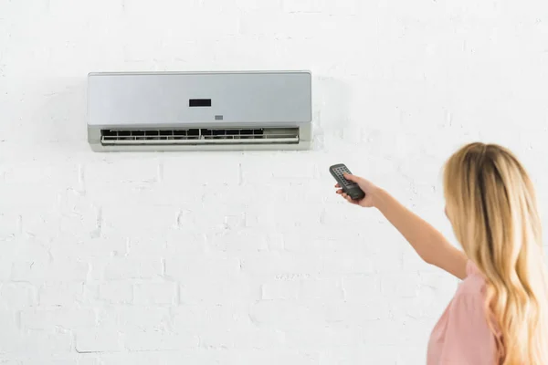 Beautiful woman suffering from heat and holding remote control under air conditioner at home — Stock Photo