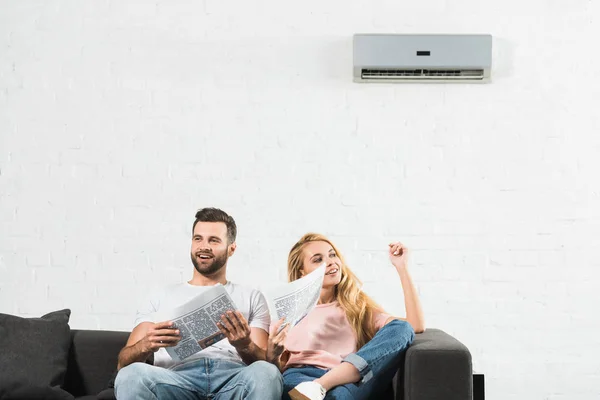 Couple sur le canapé avec des journaux souffrant de chaleur sous climatiseur à la maison — Stock Photo