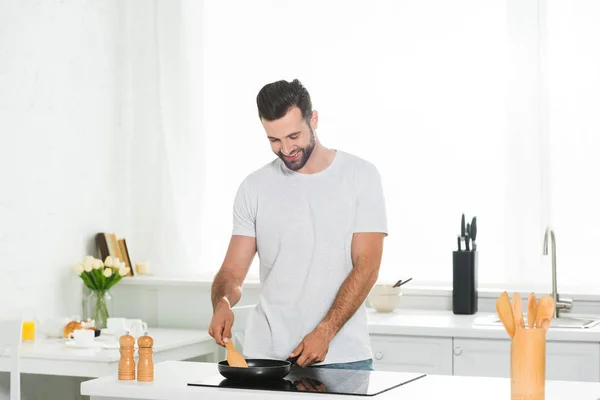 Мужчина готовит с помощью шпателя и сковороды на кухне по утрам — стоковое фото