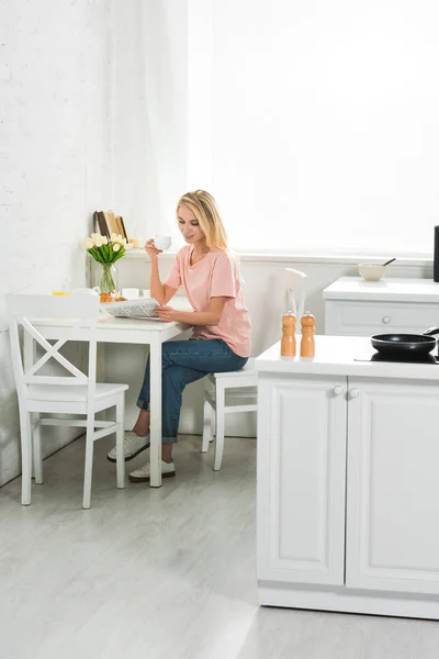 Bela mulher com xícara de café e jornal na mesa da cozinha de manhã — Fotografia de Stock