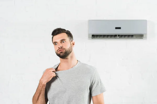 Hombre guapo que sufre de calor bajo el aire acondicionado en casa - foto de stock