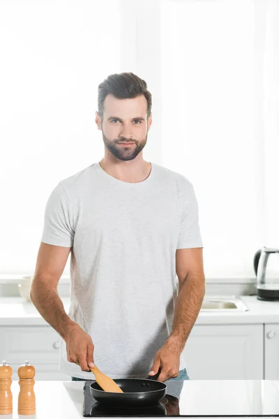 Hombre cocina con espátula y sartén en la cocina por la mañana - foto de stock