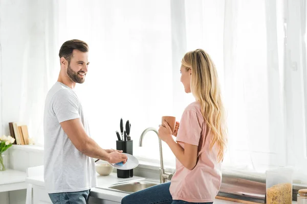 Woman with coffee cup near man washing dishes at kitchen — Stock Photo