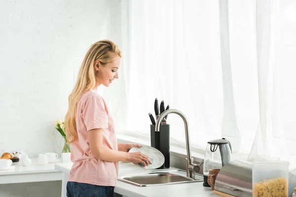 Hermosa mujer lavando platos en la cocina por la mañana - foto de stock