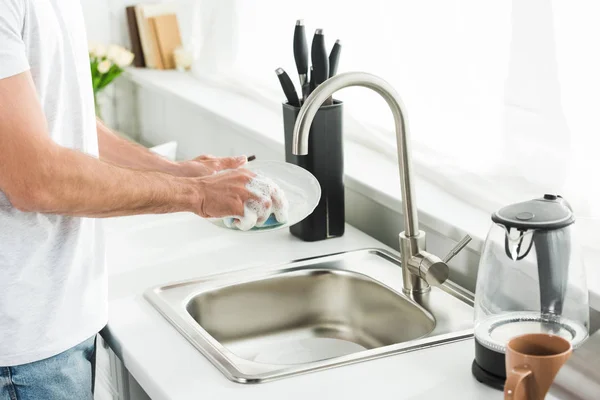 Vista recortada del hombre lavando platos en la cocina por la mañana - foto de stock