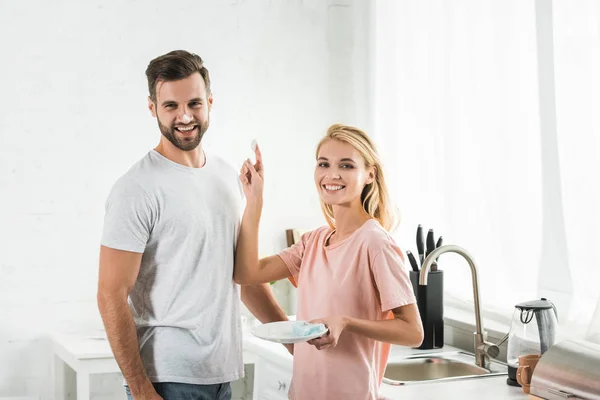 Hermosa mujer poniendo espuma en el hombre sonriente en la cocina por la mañana - foto de stock