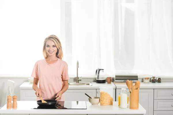 Beautiful woman cooking with frying pan and spatula at kitchen in morning — Stock Photo