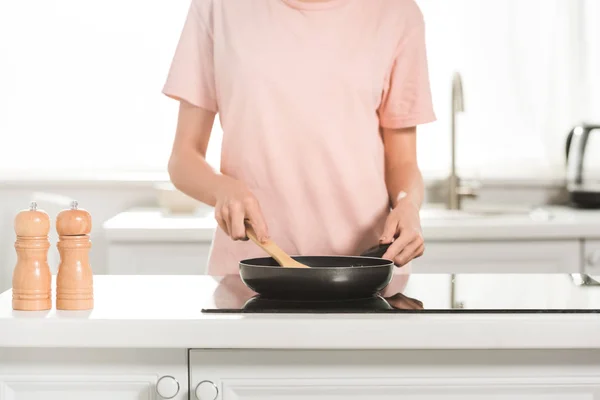 Cropped view of woman cooking with frying pan and spatula at kitchen in morning — Stock Photo