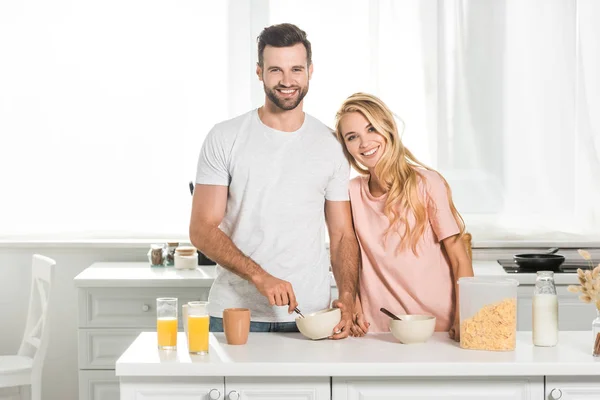 Счастливая пара с мисками хлопьев во время завтрака на кухне — стоковое фото