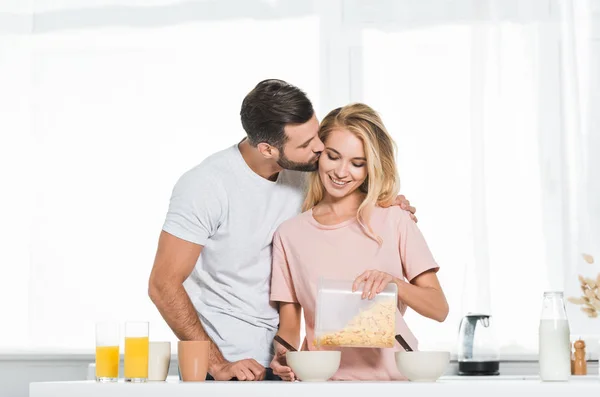 Мужчина целует женщину наливая хлопья во время завтрака на кухне — стоковое фото