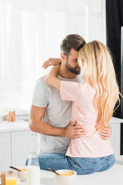 Pareja abrazándose en el mostrador de cocina durante el desayuno en la cocina - foto de stock