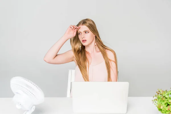 Girl suffering from heat with Electric Fan at computer desk on grey — Stock Photo
