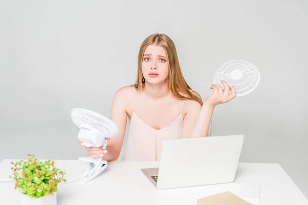 Beautiful girl holding electric fan at desk and suffering from heat on grey — Stock Photo