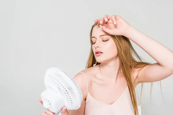 Belle jeune femme souffrant de chaleur et tenant Ventilateur électrique isolé sur gris — Photo de stock