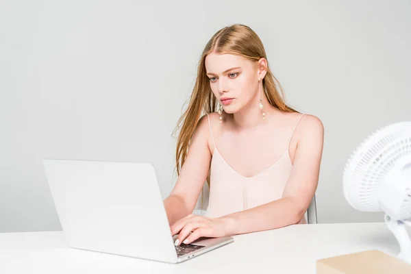 Hermosa chica usando el ordenador portátil y sufriendo de calor aislado en gris - foto de stock