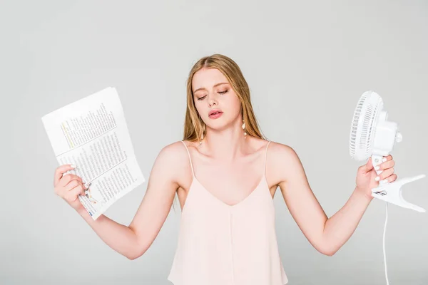 Beautiful young woman with Electric Fan and newspaper suffering from heat on grey — Stock Photo