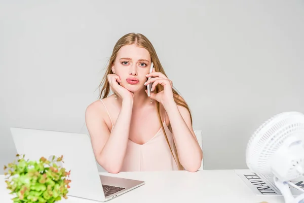 Beautiful girl talking on smartphone and suffering from heat at computer desk isolated on grey — Stock Photo