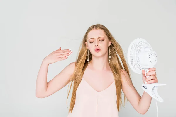 Bella giovane donna che soffre di calore, gesticolando e tenendo Ventilatore elettrico isolato su grigio — Foto stock