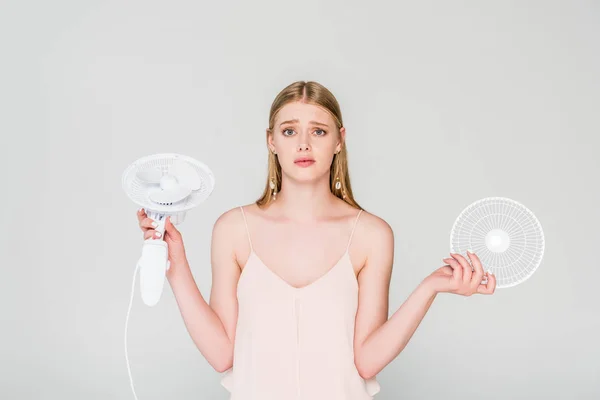 Красивая смущенная молодая женщина держит электрический вентилятор изолирован на серый — стоковое фото