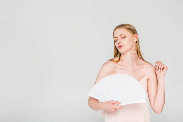 Hermosa joven con ventilador de mano que sufre de calor aislado en gris - foto de stock